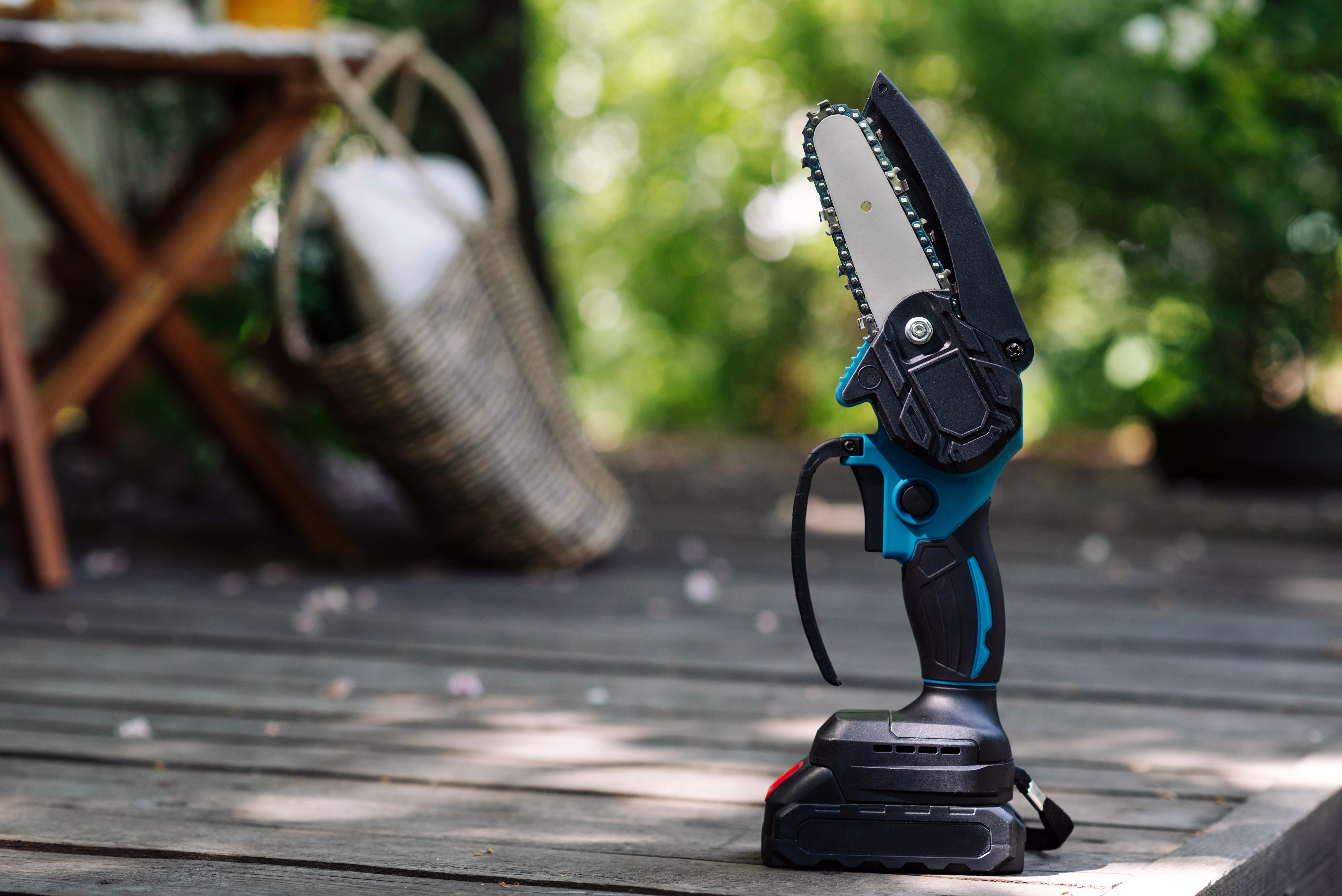 mini portable electric chain saw on summer garden background